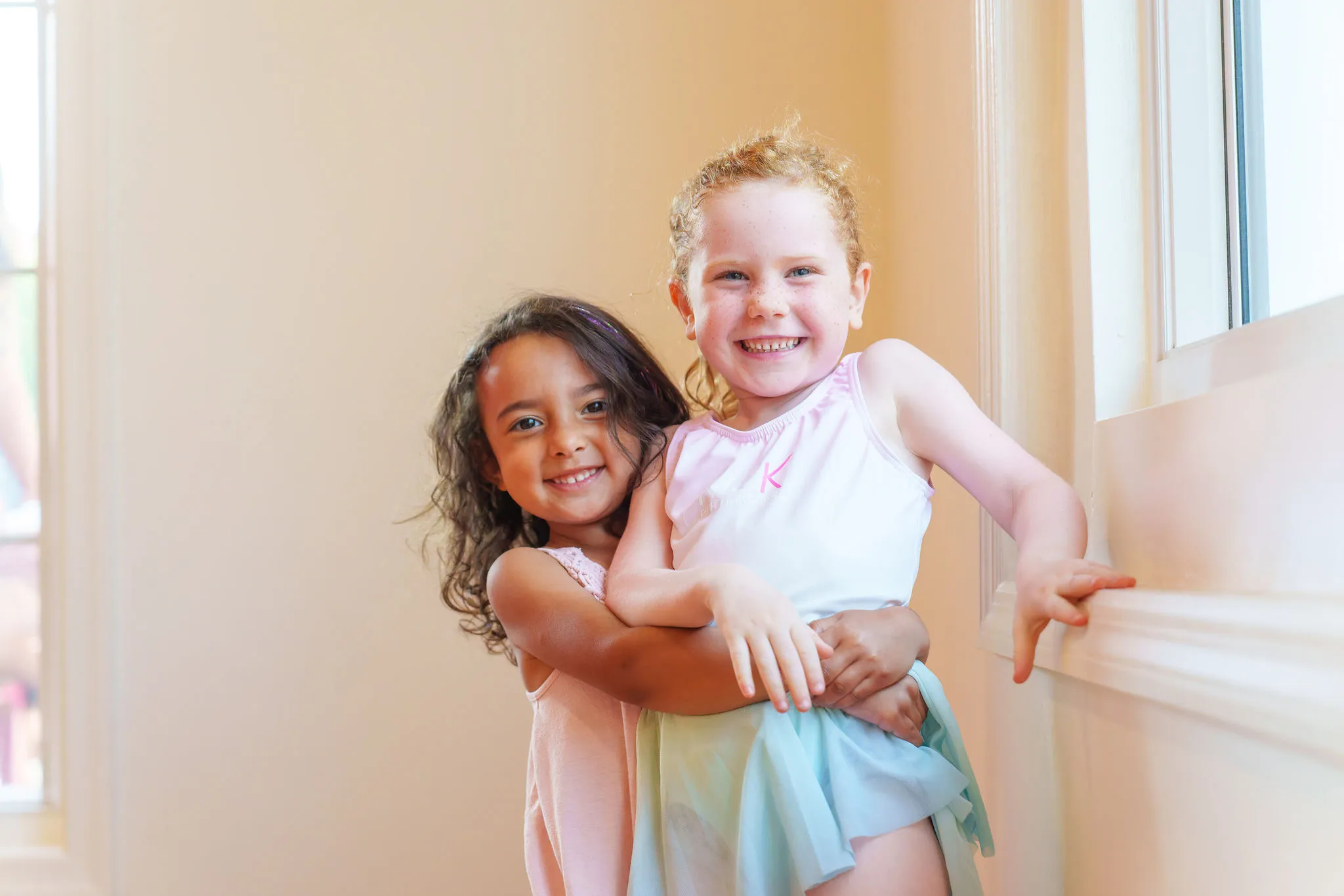 Two young KICK dancers laughing and hugging at the ballet barre