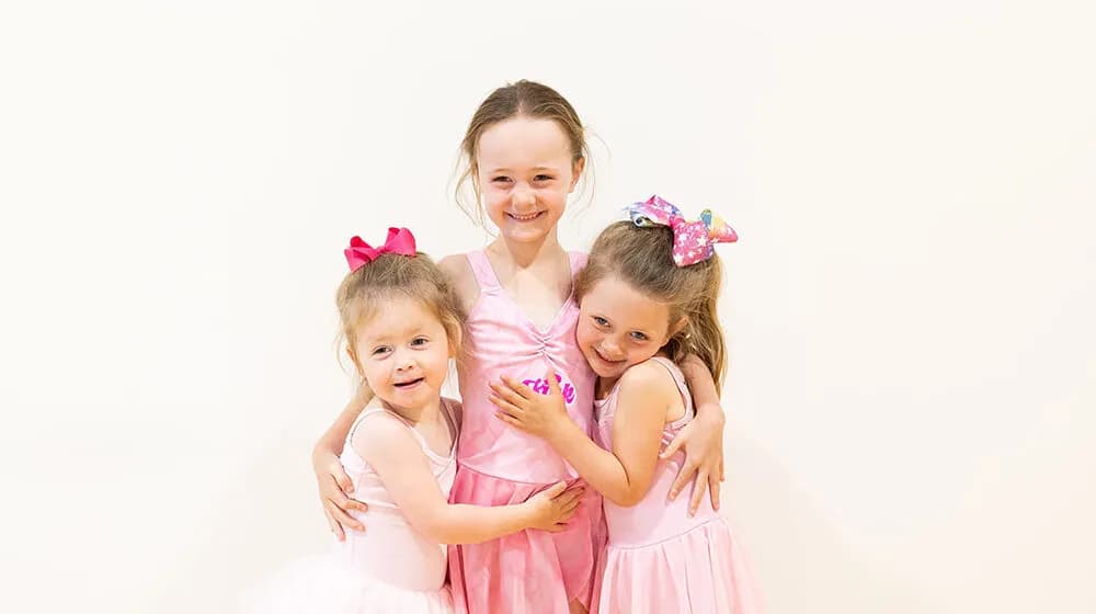 Three little KICK dancers hugging and smiling