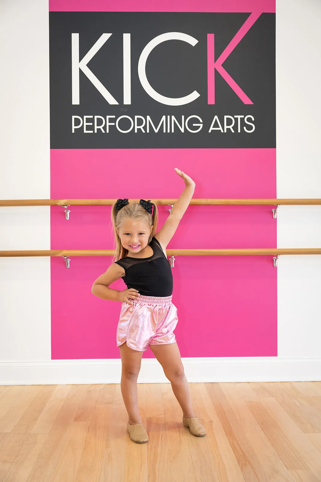 A young dancer posing proudly in front of the pink KICK Performing Arts sign